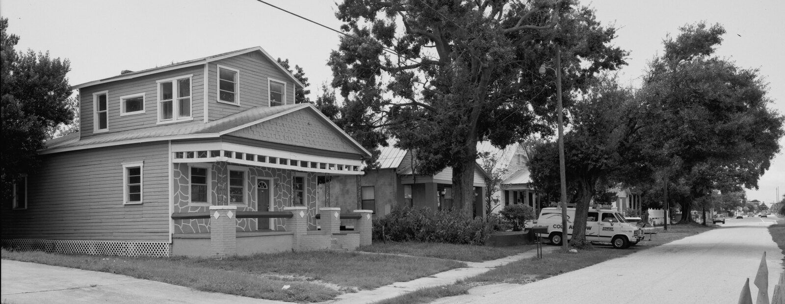 A modest two-story wood frame bungalow with a deep front porch on a quiet Tampa street, with neighboring houses receding down the block.