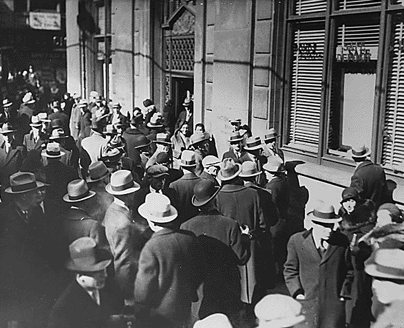 A crowd of men in overcoats and hats packed against the doors of a bank, Michigan, February 1933.